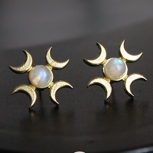 May include: A pair of gold earrings with a moon and star design. Each earring features a white moonstone in the center surrounded by five crescent moons.