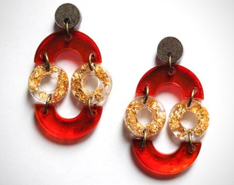 May include: A pair of red and gold earrings with a geometric design. The earrings are made of resin and feature gold leaf accents.