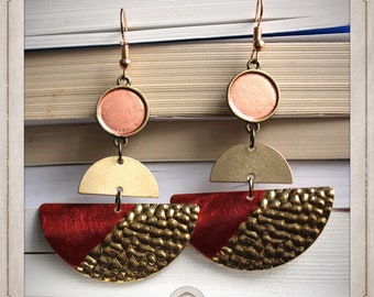 May include: A pair of gold and red geometric earrings with a hammered texture. The earrings feature a round copper disc with a gold top and a half-circle shape with a red and gold design.