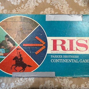 May include: Vintage Risk board game box with a blue background and the word "RISK" in red letters. The box features a map of the world divided into continents, with a red, white, and blue color scheme. The box also includes the text "Parker Brothers Continental Game".