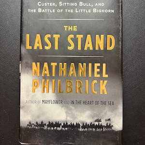 May include: A black and gold book cover with the title "The Last Stand" by Nathaniel Philbrick. The subtitle is "Custer, Sitting Bull, and the Battle of the Little Bighorn". The author is also noted as the author of "Mayflower" and "In the Heart of the Sea". The cover features a black and white photograph of a group of people on horseback.