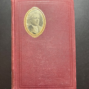 May include: A burgundy hardcover book with a gold-framed oval portrait of a man on the front cover.