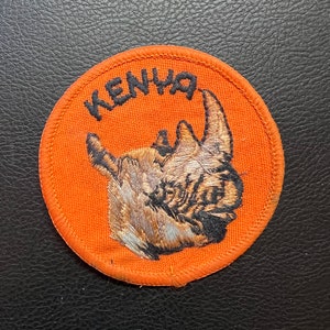 May include: Orange fabric patch with black stitching and a black embroidered rhino with the word "KENYA" in black lettering.