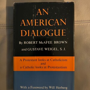 May include: A black book with the title "An American Dialogue" by Robert McAfee Brown and Gustave Weigel, S.J. The subtitle is "A Protestant looks at Catholicism and a Catholic looks at Protestantism". The book has a foreword by Will Herberg.