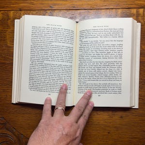 Puede incluir: Libro abierto con texto, sostenido por una mano con un anillo de oro. Las p&aacute;ginas est&aacute;n amarillentas y el texto es negro. El libro est&aacute; abierto en una p&aacute;gina con texto y n&uacute;meros.