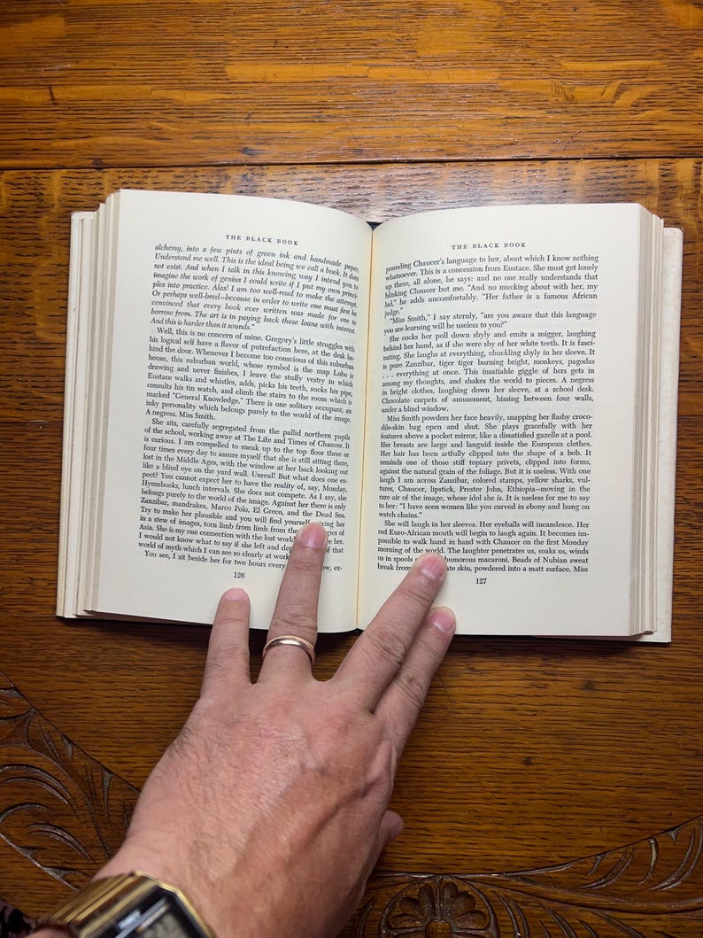 Puede incluir: Libro abierto con texto, sostenido por una mano con un anillo de oro. Las p&aacute;ginas est&aacute;n amarillentas y el texto es negro. El libro est&aacute; abierto en una p&aacute;gina con texto y n&uacute;meros.