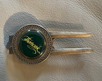 May include: A silver golf ball holder with a green and gold circular emblem that says "Thorncreek".