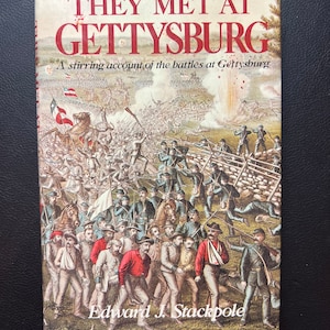 May include: A vintage book cover with a red title "THEY MET AT GETTYSBURG" and a subtitle "A stirring account of the battles at Gettysburg". The cover features a detailed illustration of a Civil War battle scene with soldiers, horses, and smoke.