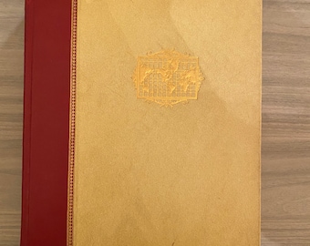 May include: A vintage book with a gold-colored cover and a red spine. The cover features a decorative design with a world map inside a frame.