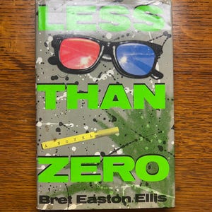 May include: Book cover for "Less Than Zero" by Bret Easton Ellis. The cover features the title in large green letters, with 3D glasses and a cigarette. The background is gray with green splatters and white paint splatters.