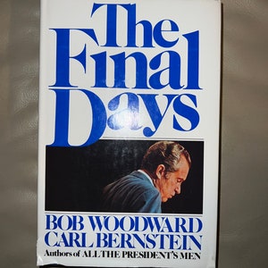 May include: A white book with the title "The Final Days" in blue text. The book cover features a black and white photo of a man in a suit looking down. The author's names are "Bob Woodward" and "Carl Bernstein" in blue text. The book is subtitled "Authors of All The President's Men".