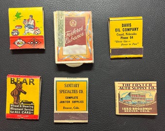 May include: A collection of vintage matchbooks with colorful designs and text. The matchbooks feature various brands and businesses, including "Davis Oil Company" and "Sanitary Specialties Co."