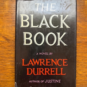 Puede incluir: Un libro de tapa dura negro titulado "THE BLACK BOOK". El t&iacute;tulo est&aacute; en blanco, el nombre del autor, Lawrence Durrell, en rojo. El libro es una novela y el autor de "Justine".