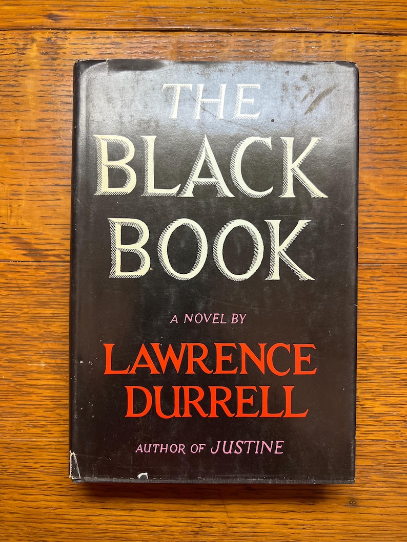 Puede incluir: Un libro de tapa dura negro titulado "THE BLACK BOOK". El t&iacute;tulo est&aacute; en blanco, el nombre del autor, Lawrence Durrell, en rojo. El libro es una novela y el autor de "Justine".
