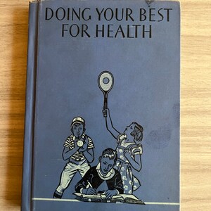 May include: A blue book with the title "Doing Your Best For Health" on the cover. The cover features a black and white illustration of three children: one playing baseball, one playing tennis, and one writing in a notebook.