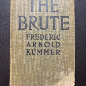 May include: A vintage book titled "The Brute" by Frederic Arnold Kummer. The book has a green cloth cover with a textured pattern.