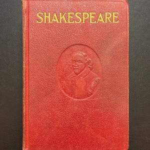 May include: A red leather-bound book with the title "SHAKESPEARE" embossed in gold lettering. The cover features a circular embossed image of William Shakespeare.