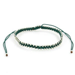 Puede incluir: Un brazalete trenzado de color verde oscuro con cuentas plateadas.