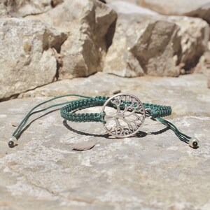 Puede incluir: Un brazalete trenzado verde con un dije de plata de árbol de la vida. El brazalete tiene dos cuentas negras en los extremos de las ataduras.