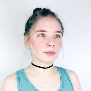 Könnte beinhalten: Eine Frau mit blaugrünem Haar trägt ein hellblaues Tanktop und eine schwarze Halskette mit einem weißen Muschelanhänger.