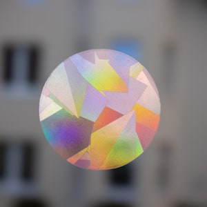 Op de afbeelding: Een ronde, iriserende sticker met een geometrisch patroon van driehoeken in tinten roze, blauw, groen, geel en oranje.