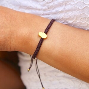 Puede incluir: Un brazalete de cordón marrón con un dije de hamsa dorado. El brazalete es ajustable y se puede usar en la muñeca o el tobillo.