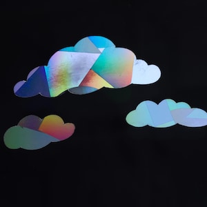 May include: Three iridescent holographic clouds in different shapes and sizes against a black background.