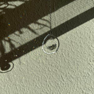 Peut inclure: Un capteur de soleil en cristal avec un anneau argenté suspendu à une chaîne. Le capteur de soleil projette des arcs-en-ciel sur un mur texturé.