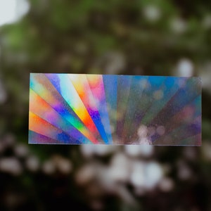 Op de afbeelding: Een rechthoekige, iriserende sticker met een regenboogpatroon. De sticker heeft een holografische afwerking en reflecteert licht in verschillende kleuren.
