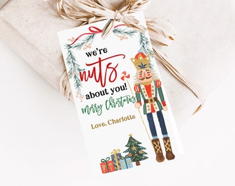 May include: A white gift tag with a watercolor illustration of a nutcracker holding a candy cane. The text reads "We're nuts about you! Merry Christmas. Love, Charlotte".