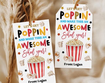 May include: Two rectangular white gift tags with brown ribbon loops. Each tag features a red and white striped popcorn bucket illustration, scattered popcorn pieces, and gold and red stars. Text reads: Let's get Poppin' and make this an Awesome School year! From: Logan.