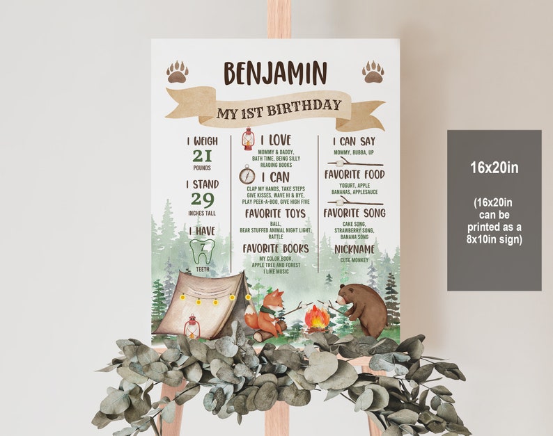 May include: A woodland-themed first birthday poster featuring a brown bear and fox sitting by a campfire. The poster includes the name Benjamin and details about the child's first year, such as weight, height, favourite foods, and songs. The poster is printed on a white background with a brown wooden frame.