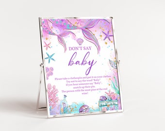 May include: A framed sign with a mermaid theme, featuring the text "DON'T SAY baby." The sign has a watercolor design with mermaid tails, seashells, and starfish in shades of purple, teal, and gold. Instructions for a baby shower game are included.