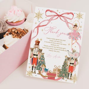 May include: A pink gift box with cupcakes and a decorative card. The card features a watercolor design with a ballerina, nutcracker, and text that reads "Thank you." The cupcakes have various toppings.
