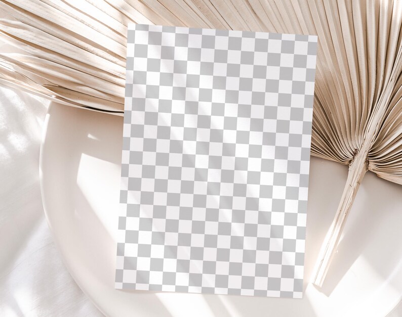 May include: A blank white card with a checkered pattern sits on a beige surface with a dried palm leaf behind it.