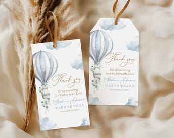 Può includere: Due etichette regalo per baby shower con un design ad acquerello di mongolfiera blu e bianca. Le etichette includono il testo "Thank you for showering our baby with love" e i dettagli del baby shower.