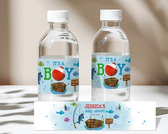 May include: Two clear plastic water bottles with blue and green labels that say "It's a Boy" with a red and white fishing bobber and a wooden boat. The labels also have a sign that says "Gone Fishing". The bottles are on a white surface with a blue and white label that says "Jessica's Baby Shower" with a fishing rod and fish.