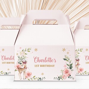 Puede incluir: Cajas de regalo rosas y blancas con un diseño floral y una ilustración de un ciervo. Las cajas tienen un asa y dicen "Charlotte's 1st Birthday" en la parte delantera.