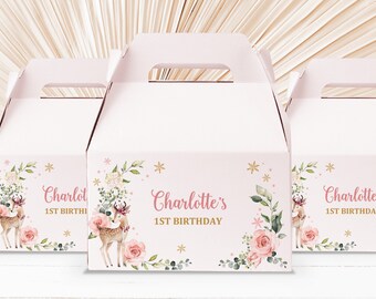 May include: Pink and white favor boxes with a floral design and a deer illustration. The boxes have a handle and say "Charlotte's 1st Birthday" on the front.