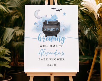 May include: A white sign with blue and black accents announcing a baby shower. The sign reads "A baby is brewing, welcome to Alexandra's Baby Shower, 10.24.25". The sign features a black cauldron with blue smoke and stars.