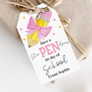 Puede incluir: Una etiqueta de regalo con una ilustración de un lápiz amarillo con una goma de borrar y un lazo rosa. La etiqueta dice "Have a PEN-dous 1st day of School From: Sophia" en rosa y negro. La etiqueta está atada a un regalo envuelto.