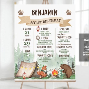 May include: A brown and green illustrated poster with a woodland theme. The poster is for a child's first birthday and includes the child's name, Benjamin, and details about their first year, such as their weight, height, favourite foods, and songs. The poster features a campfire, a tent, a fox, and a bear.