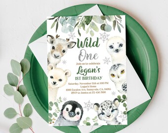 Peut inclure: Une carte d'invitation blanche avec une bordure de feuilles vertes. La carte présente un design pailleté argenté avec le texte "Wild One" et "Logan's 1st Birthday". La carte présente également des illustrations de différents animaux, dont un ours polaire, un pingouin, un phoque, un hibou et un léopard des neiges.