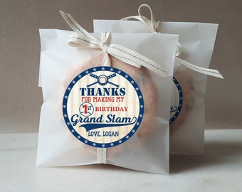 May include: White favor bags with a blue and red baseball-themed sticker that says "Thanks for making my 1st birthday a Grand Slam. Love, Logan."