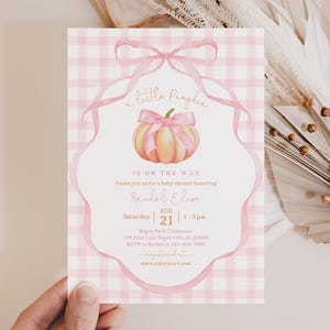 Puede incluir: Una tarjeta de invitación rectangular para baby shower con un fondo de cuadros vichy en rosa claro y blanco. El centro muestra una calabaza en acuarela con un lazo rosa, enmarcada por una ilustración de cinta rosa. El texto incluye a little Pumpkin.