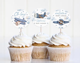 May include: Three blue and white cupcake toppers with airplane designs. The toppers say "Oh boy!" "Stephanie's Baby Shower" and "Welcome Baby Logan".