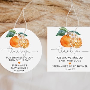 May include: Two round thank you tags with a watercolor illustration of an orange slice and a whole orange with green leaves. The text on the tags reads "Thank you for showering our baby with love" and includes the name of the baby shower and the date.