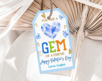 Może przedstawiać: Jasnoniebieska etykieta prezentowa z brązowym sznurkiem. Etykieta zawiera niebieskie serce z klejnotu, napisy "YOU ARE A GEM OF A FRIEND" i "Happy Valentine's Day". Etykieta jest podpisana "Love, Logan".