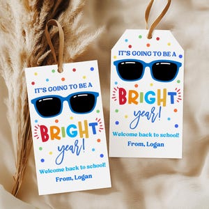 May include: Two rectangular white gift tags with brown ribbon loops. Each tag features blue sunglasses, colorful polka dots, and the text: IT'S GOING TO BE A BRIGHT year! Welcome back to school! From, Logan. The design uses red, yellow, and blue lettering.