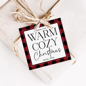 May include: A wrapped gift with a raffia bow and a tag that reads "Wishing You a Warm & Cozy Christmas From, Anne." The tag has a red and black buffalo plaid border.